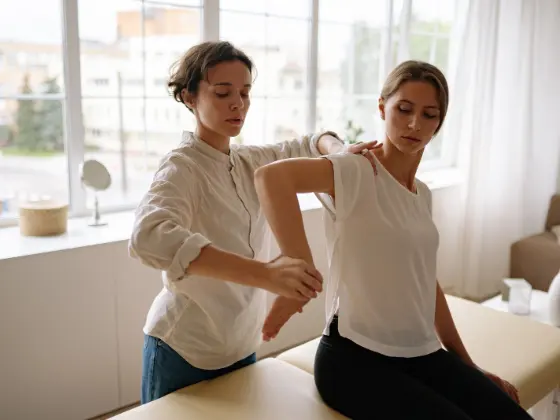 Fisioterapeuta avaliando a postura dos ombros de uma paciente em pé.